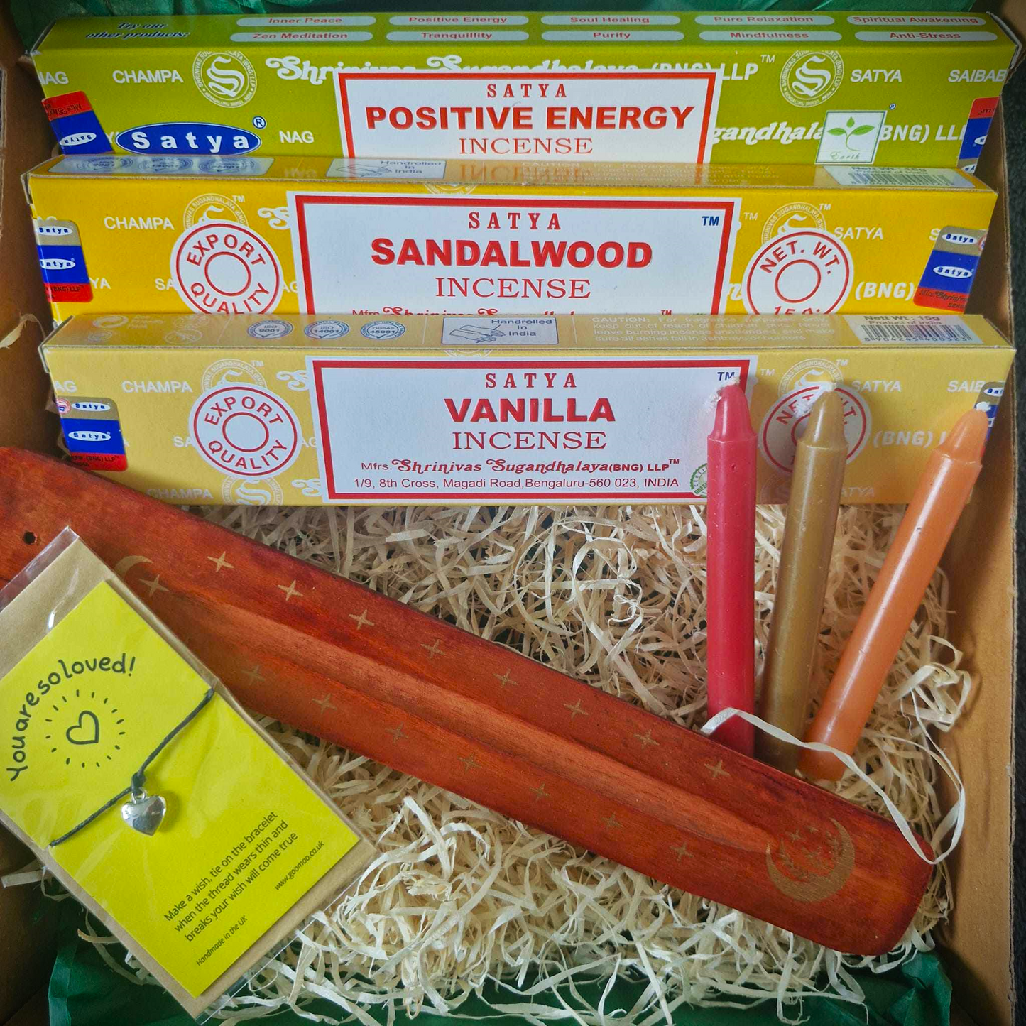 This picture shows the inside of the Happiness Incense Gift Box. Inside, there are 3 incense stick packages. This one contains Positive Energy, Sandalwood and Vanilla. There are 3 spell candles, an ash catcher and a wish Bracelet.