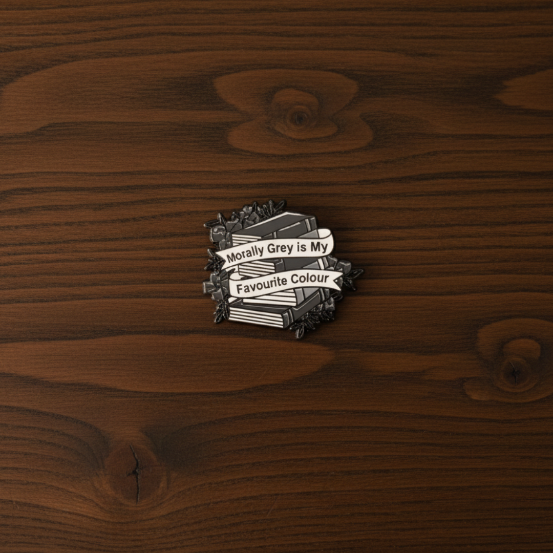 An enamel pin badge of a greyscale stack of books that says "Morally Grey is my favourite Colour"