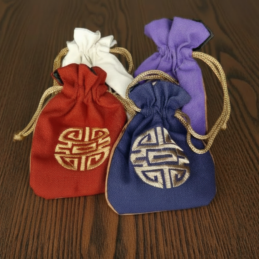 Four drawstring bags in red, white, purple, and blue with gold embroidered symbols on a dark background.