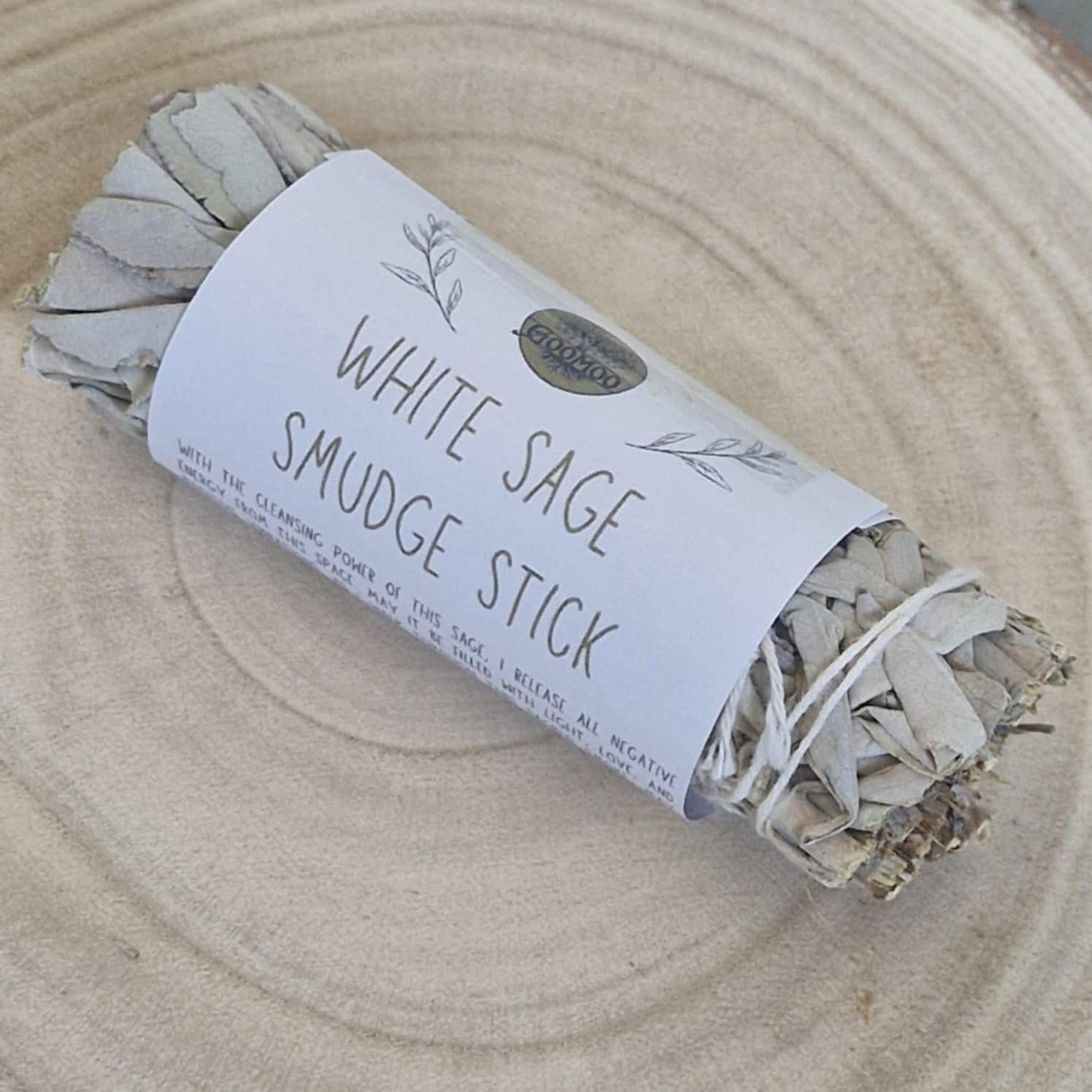 White sage smudge stick wrapped in paper with branding on a wooden surface