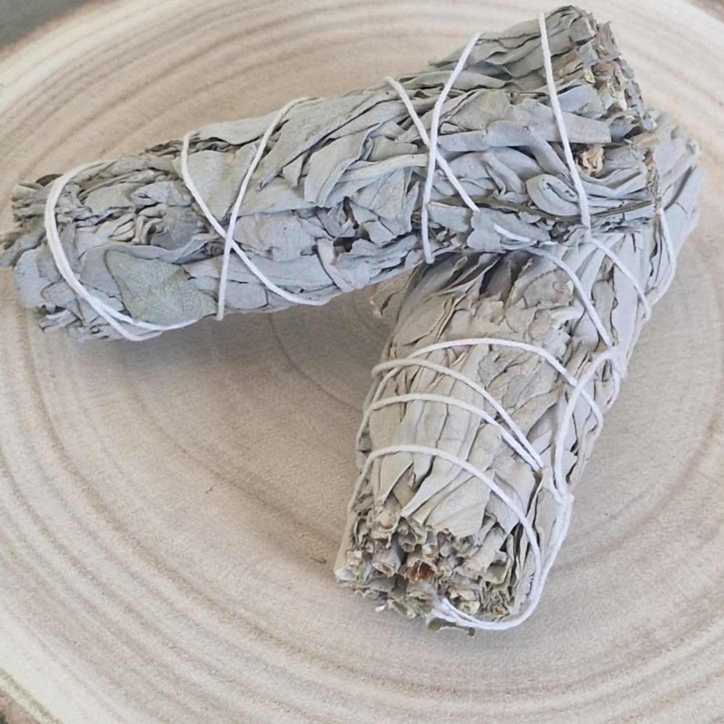 Two sage smudge sticks tied with white string on a light wooden surface