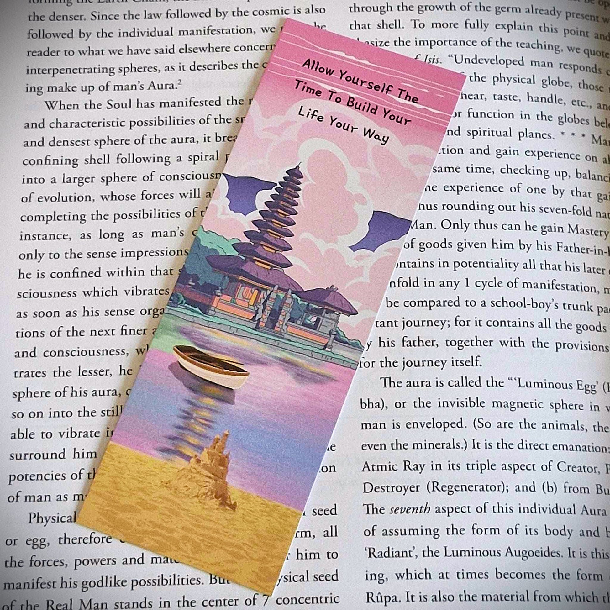 A bookmark with the words Allow Yourself The Time To Build Your Life Your Way. This affirmation bookmark is primarily pink with an asian inspired temple over a lake with a row boat on it. 