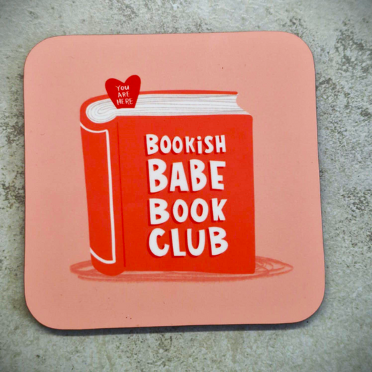 This coaster is pink with a red book on it. On the cover of the book says the words "Bookish Babe Book Club".