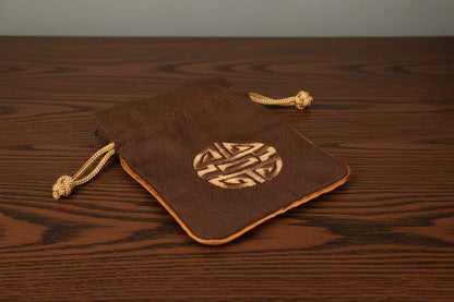 Brown Dungeons and Dragons dice drawstring pouch with a gold emblem on a black surface