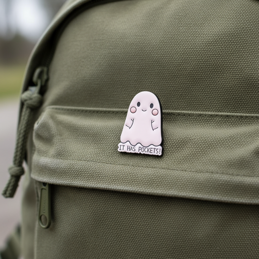 Pink ghost charm with 'It has pockets!' text on a green backpack