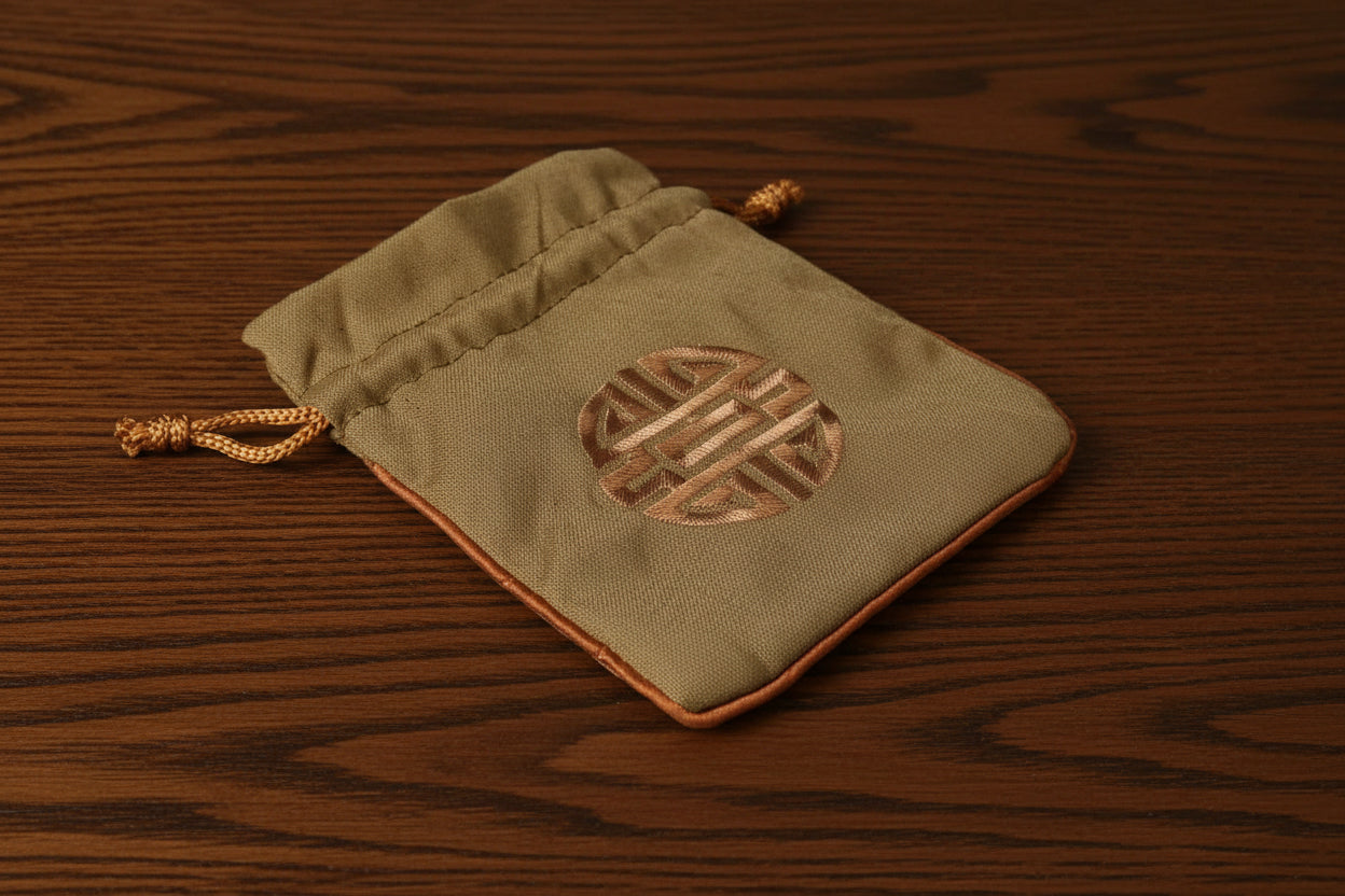 Small Green drawstring pouch with a central emblem on a dark oak table