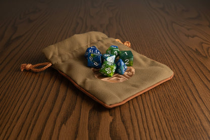 Green drawstring bag with polyhedral dice on a dark oak table