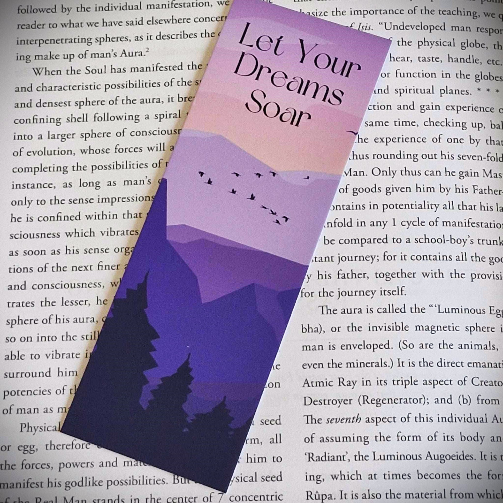 A bookmark with the words Let Your Dream Soar. This affirmation bookmark is primarily purple. In the foreground are silhouette trees, and behind are purple mountains with Birds flying over them.