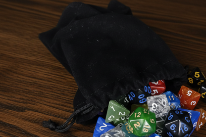 Colorful polyhedral dice spilling out of a black drawstring bag on a yellow surface.