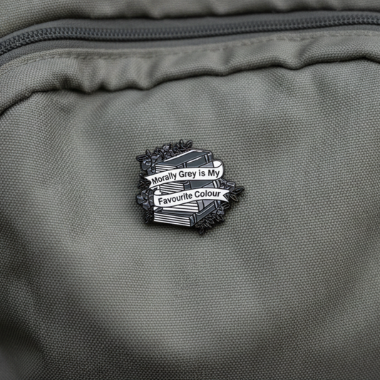 An enamel pin badge of a greyscale stack of books that says "Morally Grey is my favourite Colour"