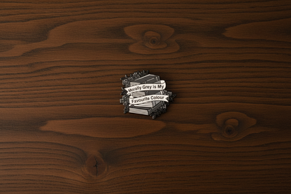 An enamel pin badge of a greyscale stack of books that says "Morally Grey is my favourite Colour"
