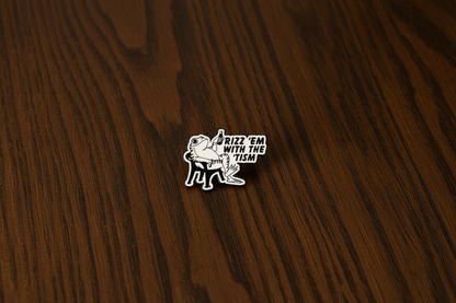 An enamel Pin badge that has a picture of a frog sitting in a chair, holding a bottle saying Rizz 'em with the 'tism on a dark oak table