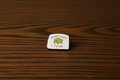 An enamel Pin Badge with a poorly drawn frog on it that says, sometimes I Think on a dark oak table
