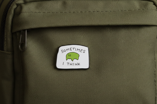An enamel Pin Badge with a poorly drawn frog on it that says, sometimes I Think on a backpack