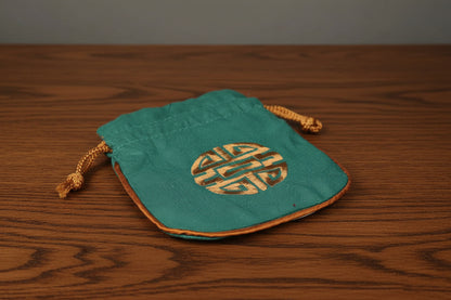 Green drawstring pouch with gold emblem on a dark oak table