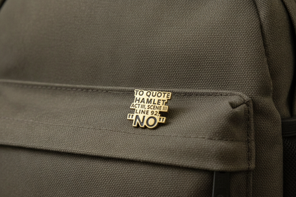 An enamel Pin badge that says to quote Hamlet Act III, Scene III, Line 92, "NO". on a green Backpack.