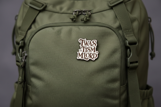An enamel Pin badge that says TWAS THE TISM, M'LORD. In black writing on a green backpack