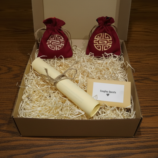 Gift set with red drawstring bags, a rolled paper, and a card labeled 'Couples Quests' on a bed of straw.
