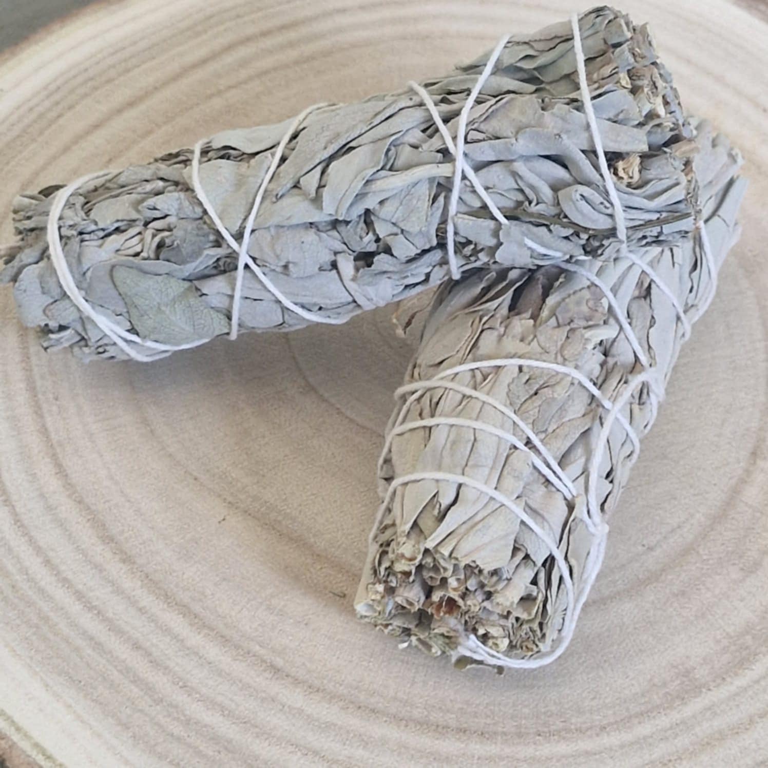Two sage smudge sticks tied with white string on a light wooden surface