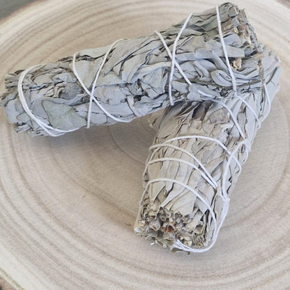 Two sage smudge sticks tied with white string on a light wooden surface